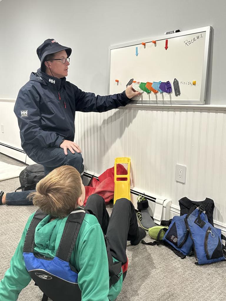Coach using the Opti kit on a whiteboard with young sailors